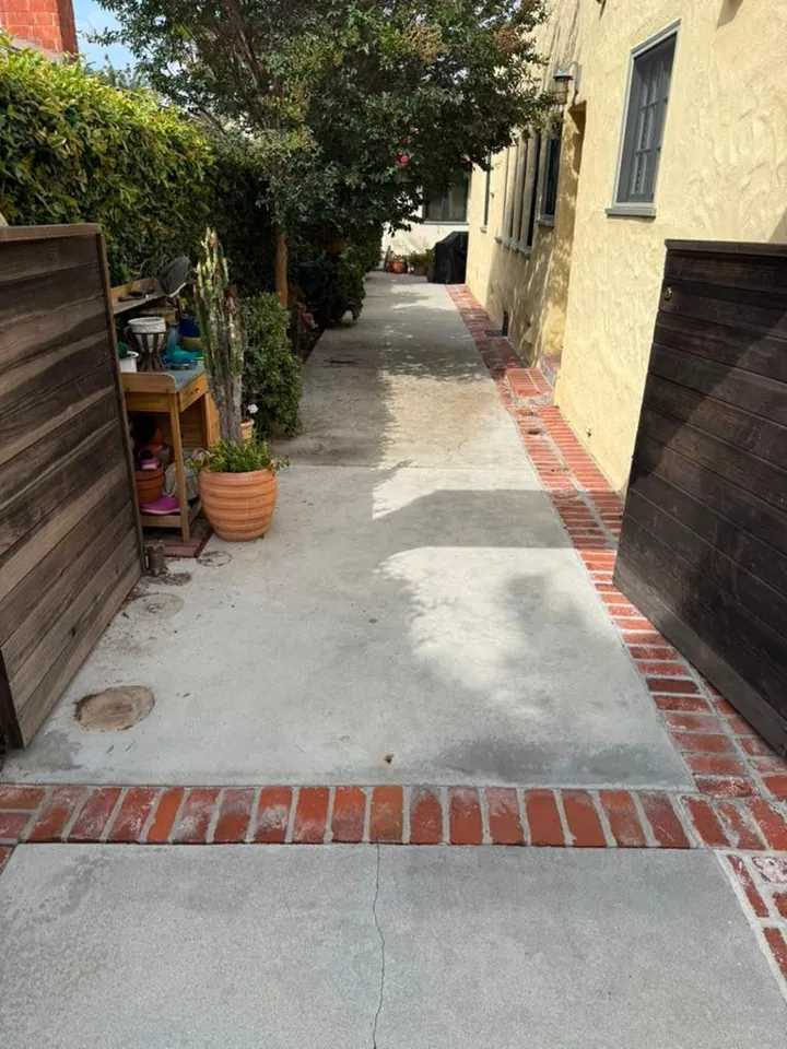 Clean, dry side-yard concrete walkway with brick border after professional cleaning