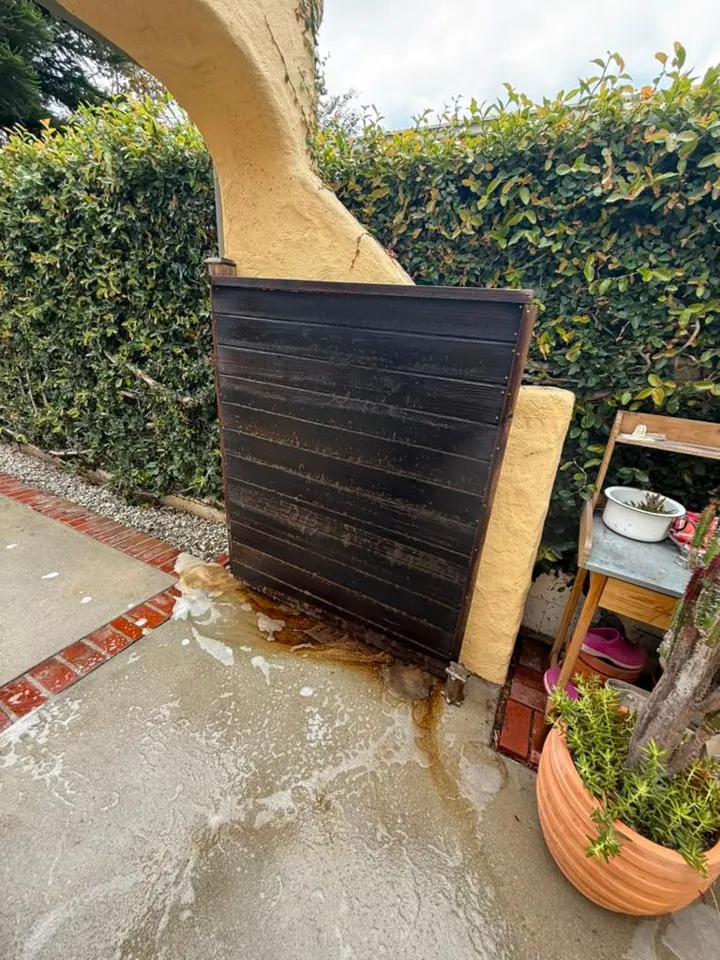 Dark-stained wood gate panel under a stucco arch during cleaning